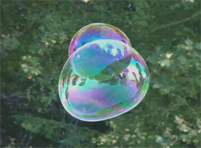 Iridiscencia en pompas de jabón. Fuente: https://commons.wikimedia.org/wiki/File:Soap_Bubble_-_foliage_background_-_iridescent_colours_-_Traquair_040801.jpg.