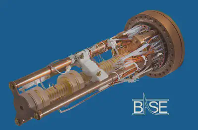 Imagen de una [**trampa de Penning**](https://es.wikipedia.org/wiki/Trampa_de_Penning). Sobre un fondo azul tenemos una máquina con base marrón con dos pilares más otro que se intuye al fondo con una espiral dorada dentro. Esta espiral está conectada por una gran cantidad de cables. Fuente: https://cds.cern.ch/record/2748764